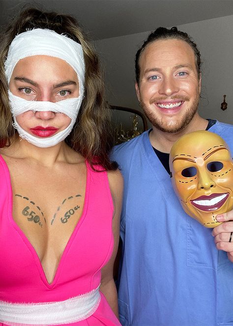 man wearing doctor's scrubs and holding a plastic halloween mask smiles while standing next to a woman in a pink dress, surgery marks on her skin, red lipstick, and bandages on her face covering a bruised nose Scar Face Costume Couple, Plastic Surgeon And Patient Costume, Mummy Costume Couple, Plastic Surgery Costume, Ideas For Cosplay, Plastic Surgery Makeup, Surgery Makeup, Scooby Doo Dress, Mummy Makeover