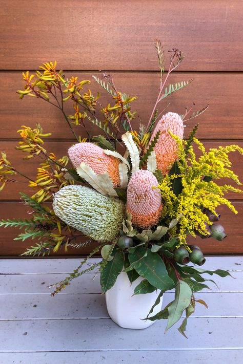 bright banksias, yellow goldenrod and textural gumnuts spaced together in a white vase against a brown wooden wall background. Australian Native Flowers In Vase, Paint Reference, Unique Floral Arrangements, Australian Native Flowers, Native Flowers, Australian Native Plants, Australian Flora, Plant Decor Indoor, Australian Native