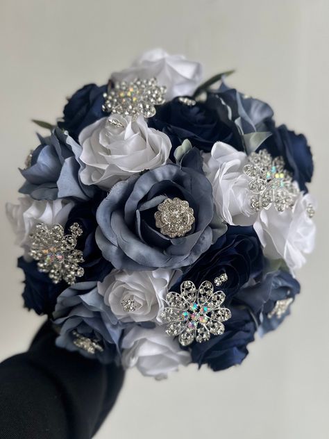 Handmade quinceañera bouquet with navy blue, dusty blue and white color shade of roses. Finished off with silver brooches.  *Please note brooches can change in style based on availability*   Decor can be changed upon request.  *This is a made to order bouquet* Wedding Bouquets Dark Blue, Navy Blue Quince Bouquet, White Quinceanera Bouquet, Navy Blue Quinceanera Ideas Decor, Navy Quince, Navy Blue Quinceanera Ideas, Quinceanera Navy Blue, Navy Blue Quince, Blue Quinceanera Ideas