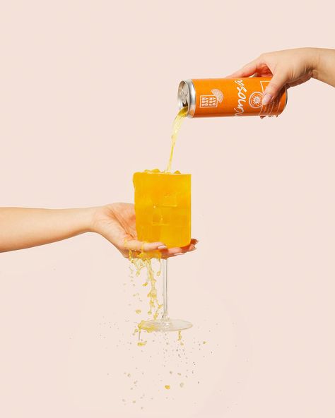 A peach background with a can of Sunday Funday mimosa being poured into a stemmed glass. The liquid is overflowing and spilling down the bottom of the glass. A hand is holding the can and another hand is holding the glass. Drink Photoshoot, Beverage Photography Ideas, Cocktail Mixology, Beverage Photography, Juice Branding, Drinks Packaging Design, Cocktail Photography, Drinks Brands, Orange Soda