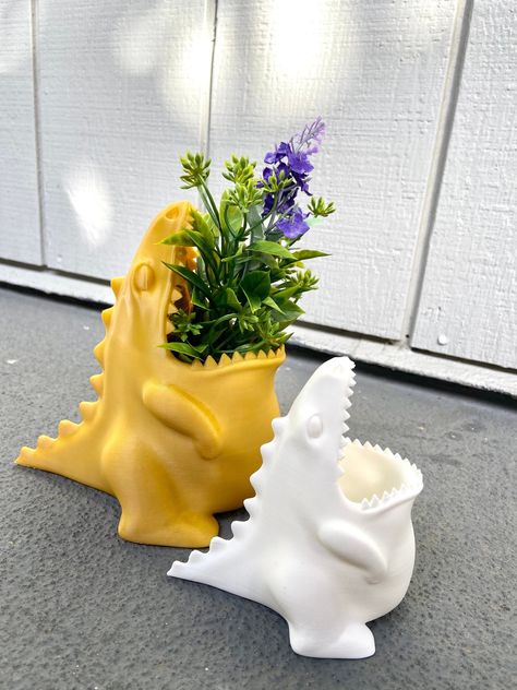 👉👉 Looking for some Jurassic charm to spice up your home decor or office? Look no further than our hungry dinosaur collection! First, meet our new best friend, the Dinosaur Planter! He's so hungry for sunlight, that he'll make sure your plants get all the light they need to grow big and strong. This little guy is just raring to go and ready to hold your favorite plant! With his big mouth, he'll chomp down on any small succulent or flower you give him. Just don't forget to water him or he might Dinosaur Home Decor, Dinosaur Planter, Dinosaur Collection, Cooking Utensil Holder, Cool Dinosaurs, First Meet, Cooking Utensil, Types Of Plastics, Kitchen Cooking Utensils