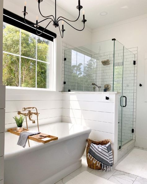 Brass wall mounted faucet with hand shower is mounted over a white freestanding tub framed by a white shiplap surround. A glass half wall shower with door next to the tub is clad in white staggered tiles. Freestanding Tub Surround, Sandcloud Towel, Tub Next To Shower Ideas, Stand Alone Bath Tub, Half Wall Shower, White Tile Shower, Struggle Bus, New House Bathroom, Stand Alone Tub