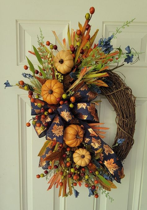 Welcome the beauty of autumn into your home with this handmade Fall Harvest Pumpkin Wreath. This stunning wreath is crafted on a sturdy grapevine base, adorned with a lush arrangement of pumpkins, berries, and fall leaves in vibrant shades of orange, green, and gold.     Perfect for your front door, mantel, or ad a centerpiece, this wreath brings a touch of seasonal charm to any space. Whether you're decorating for Thanksgiving or simply love the colors of fall, this wreath is an ideal choice.      This wreath is meticulously handcrafted to ensure high-quality and durability. The pumpkins and berries add  delightful pop of color, while the realistic leaves create a natural, rustic look. The navy blue ribbon with copper leaves enhances the overall design, making it a unique addition to your Fall Wreaths Ribbon, Front Door Wreath Ideas, Decorating For Thanksgiving, Autumn Door Decor, Wreaths Ribbon, Diy Fall Wreath Ideas, Wreath With Pumpkins, Door Wreath Ideas, Elegant Fall Wreaths