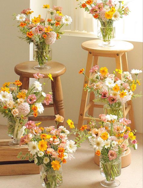 6 vases full of flowers displayed on wooden stools and such. The flowers are white, yellow, and dusty pink with hints of orange. They arranged in a garden style with a  wild whimsical look. Daisy Flower Arrangements, Yellow Cosmos, Pink Lisianthus, Yellow Flower Arrangements, Yellow Bouquets, Daisy Wedding, Floral Aesthetic, Gerber Daisies, Pink Wedding Flowers