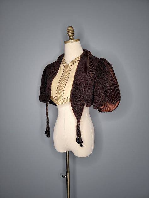 This vintage costume piece is BEAUTIFUL! It looks like a cape, but I believe it would be classified as a bolero, as it does have arm holes. The body is made from a thick chocolate colored carpet-like fabric. It is a layered piece with a cream-colored attached vest underneath. It has an ornate trim at the shoulders and a fringe in front. I'm not certain of the age of this bolero. The backstory that came with it, is that it came from an old theatre and is presumed to be from the Mid Century.  Hand Vintage Cape For Costume, Vintage Cape For Costume Outerwear, Vintage Winter Capelet, Old Theatre, Victorian Bolero Jacket, Vintage Bolero, Theatre Outfit, Theatre Costumes, Chocolate Color