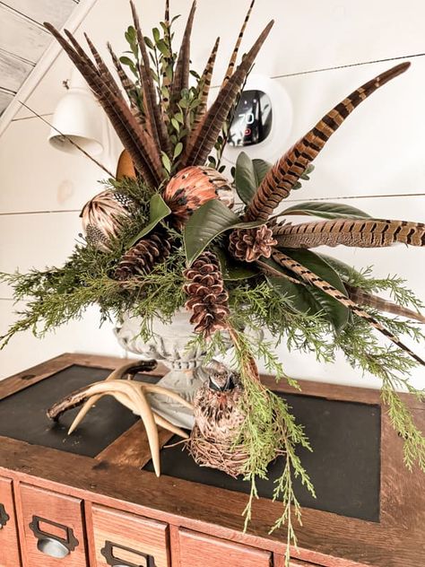 Pheasant feathers and ornament combine with pinecones and greenery for a table centerpiece. Pheasant Feather Decor, Christmas Centrepiece Ideas, Antler Centerpiece, Winter Mantel Decor, Woodland Centerpiece, Floral Antlers, Antlers Decor, Greenery Centerpiece, Feather Centerpieces