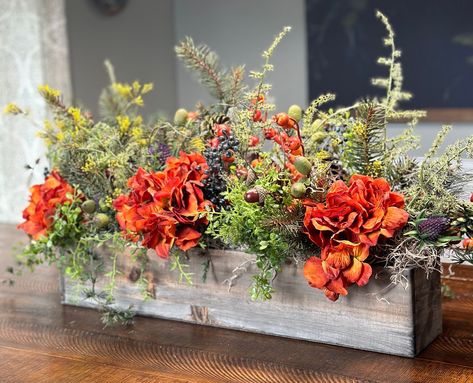 Add a touch of cozy autumn farmhouse charm to your home with this rustic style grey washed rectangular box. Filled with a delightful mix of pine, ferns, rust hydrangeas, berries, acorns, pinecones, and thistle, this arrangement is perfect for adding a warm and inviting feel to your fall decor. Whether placed on your mantel, side table, or as a stunning Thanksgiving table centerpiece, this arrangement is sure to bring a sense of the harvest season indoors. Floral Box Centerpiece, Wood Box Floral Arrangements, Fall Flower Box Arrangements, Small Fall Floral Arrangements, Rustic Dinner Table Decor, Fall Vase Decor, Farmhouse Flower Arrangements, Fall Centerpieces Wedding, Patio Table Centerpiece