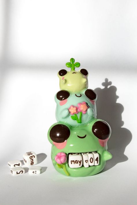 Cute spring frogs cuties holding flowers and sprout perpetual calendar perfect for desk and home decoration. Comes with clay basket and clay cubes for the months and numbers. ✿ d i m e n s i o n s ✿ Weight: 8 oz Height:  4.5 in Width: 2.5 in ✿ p r o c e s s ✿ This is a handmade creation, meticulously crafted with air dry clay. They undergo a process of sculpting, sanding, painting, and glazing right in home. Due to their artisanal nature, slight variations in color or shape are part of the charm, ensuring that each piece is truly one-of-a-kind! ✿ c a r e ✿ While air dry clay is robust, it's essential to handle it gently. Avoid bending or twisting the piece, and take care to prevent dropping them on hard surfaces. Limit exposure to water and keep them away from oils, lotions, and perfumes t Air Clay Fairy House, Cactus Clay Art, Clay Mini Calendar, Clay Water Bottle, Air Dry Clay Mini Figures, How To Color Air Dry Clay, Clay Office Decor, Cute Polymer Clay Ideas Kawaii, Colored Clay Ideas