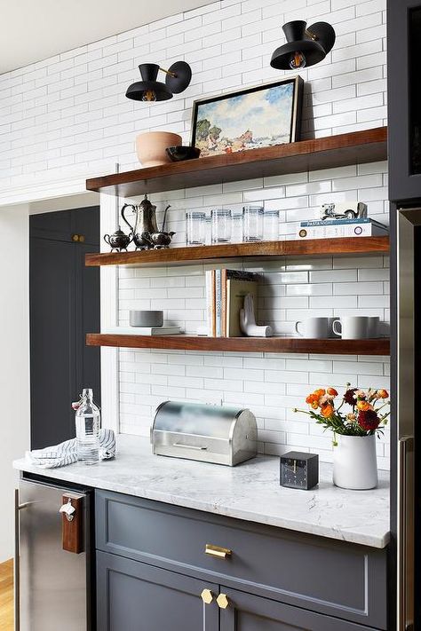 Brown wooden floating shelves are stacked against white subway backsplash tiles beneath black sconces and over gray shaker cabinets. Ikea Floating Shelves, Kitchen Floating Shelves, Floating Shelves Living Room, Floating Shelf Decor, Floating Shelves Kitchen, Shelves Ideas, Floating Shelves Bathroom, Wooden Floating Shelves, Regal Design