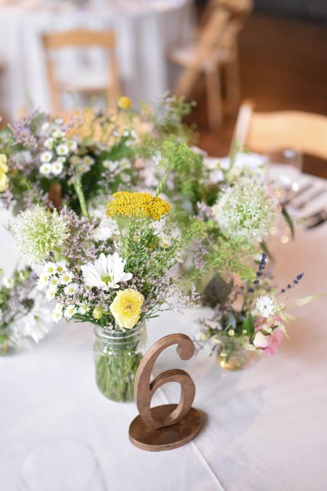 Summer lush and overflowing centerpiece in jar filled with wild and textured mix of greens, with yellow, lavender and white flowers in jar. Rustic and natural. Lavender And Green Wedding Centerpieces, Sage Green And Lavender Wedding Wedding Table Decor, White Yellow Lavender Wedding, Lavender Sage Sunflower Wedding, Lilac Rustic Wedding Table Decor, Yellow Flower Centerpieces, White Wedding Centerpieces, Wedding Arch Flowers, Flowers In Jars