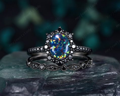 Ring details- Main Ring:  -Center stone: 6x8mm oval cut lab black opal -Side stones: black moissanite -Smooth tapered band. - Material: silver/10k white gold/14k white gold/18k white gold, coated with black rhodium Wedding band: -Accent stone: black moissanite -Band Width (Bottom): 1.6-1.7mm - Material: silver/10k white gold/14k white gold/18k white gold, coated with black rhodium --Black gold plated: What is it? How long does it last? Plating is simply a metal coating that goes on top of anothe Luxury Black Opal Engagement Ring, Black Opal Engagement Ring, Black Wedding Ring, Lab Black, Opal Engagement Ring Set, Unique Engagement Ring Settings, Black Wedding Rings, Opal Engagement Ring, Black Halo