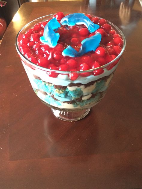 Jaws themed shark trifle. Angel food cake with blue food coloring, cheesecake Jello pudding, chocolate graham cracker goldfish & whipped cream w/blue food coloring. Topped with cherry pie filling & shark gummies. Blue Jello With Fish, Shark Cheesecake, Shark Cookie Cake, Trifle Angel Food Cake, Shark Gummies, Week Snacks, Cheesecake Jello, Shark Week Recipes, Shark Food