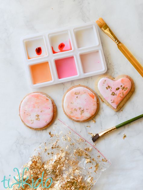 Sugar cookies coated in royal icing, painted with food coloring in tray above the cookies, bag of gold leaf and paint brush below. Painted Sugar Cookies, Cookies Bag, Garden Cookies, Watercolor Cookies, Bag Of Gold, Edible Gold Leaf, Shortbread Biscuits, Leaf Cookies, Paint Cookies