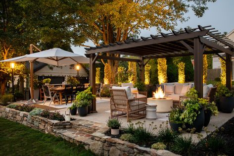 We designed this outdoor living space with both family gatherings and quiet evenings at home in mind. This client loves gardening, so we created a two foot perimeter inside the wall and filled it with perennials  - this gives the feeling as though they are sitting amongst the garden.  A pergola over the conversation area and a large cantilevered umbrella over the dining area provide relief from the sun during the daytime; a firepit and accent lighting give this patio a beautiful evening glow. Gazebo Decorating Ideas Backyard, Patio Gazebo Decorating Ideas, Gazebo Decorating Ideas, Gazebo Decorations, Conversation Area, Outdoor Gazebo, Backyard Gazebo, Patio Inspiration, Backyard Renovations