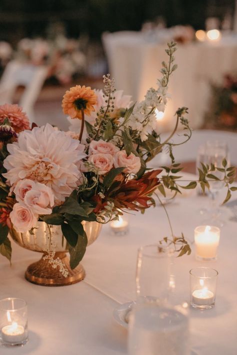 large sized vase overflowing with blooms as a wedding table centerpiece surrounded by small candles Fall Dahlia Centerpiece, Fall Elegant Tablescapes, Dahlia Decoration Wedding, Autumn Tablescapes Centerpieces, Circle Table Floral Centerpiece, Terracotta Wedding Floral Arrangements, Wedding Flower Arrangements Autumn, Dahlia Table Centerpieces, Copper Vase With Flowers