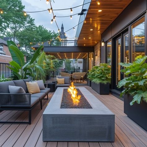 This inviting outdoor living space is the epitome of relaxation and elegance. As dusk settles, the warm glow from the modern fire pit casts a welcoming ambiance, complemented by the soft luminescence of overhead string lights. Plush seating arrangements invite guests to linger, surrounded by lush potted plants that bring a touch of nature to this sophisticated deck. The cohesive design of wood, textiles, and greenery creates a perfect backdrop for intimate gatherings or solitary repose. Modern Outdoor Living Space, Outdoor Evening, Modern Fire Pit, Outdoor Patio Space, Outdoor Comfort, Cozy Outdoor, Decks Backyard, Backyard Deck, Deck Furniture