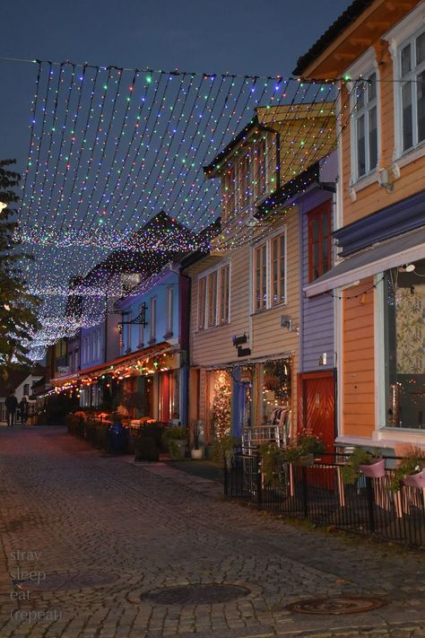 Twinkle lights shimmer over a cobblestone walkway lined with colorfully painted buildings. Norway City, Norway House, Stavanger Norway, Colourful Buildings, Norway Travel, Stavanger, Dream Holiday, Winter Pictures, Stockholm Sweden