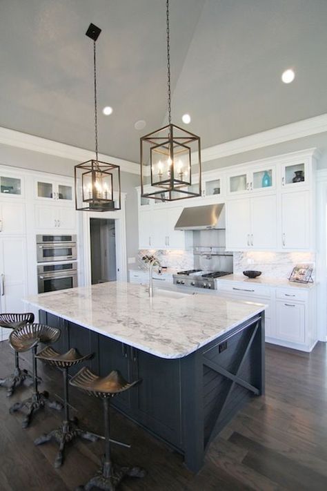 White and navy kitchen features iron and glass cage lanterns over navy center island accented with x trim moldings topped with white and gray stone countertops lined with Restoration Hardware Tractor Seat Barstools atop dark floors. A row of small glass-front cabinets are stacked over white shaker cabinets paired with white and grey stone countertops and matching backsplash. A stainless steel hood over swing-arm pot filler on stainless steel back splash above integrated gas range. Island Seating, Navy Kitchen, Decor Pad, White Shaker Cabinets, White Kitchen Island, Color Decor, Small Kitchens, Kitchen Island Design, Kitchen Redo