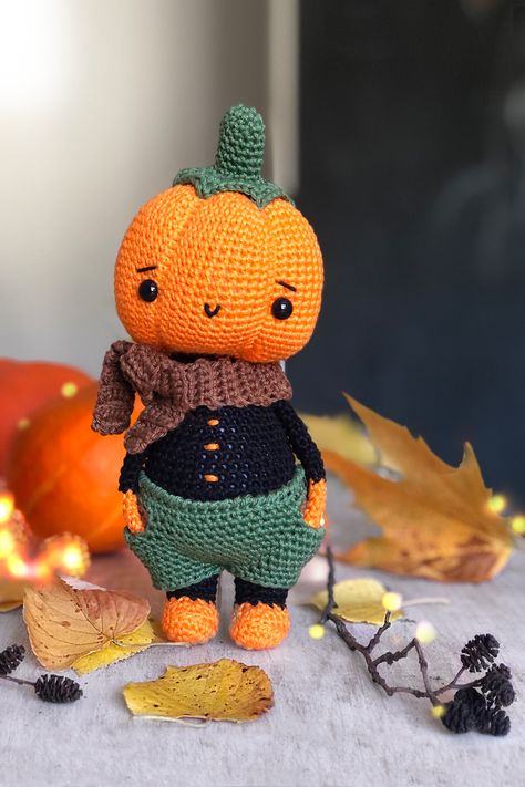 Crochet pumpkin doll, standing on the table, ready to serve as a Halloween decor. Some yellow leaves lare scattered nearby, a reminder that autumn has arrived. Crochet Halloween Costumes, Pumpkin Amigurumi, Crochet Halloween Costume, Pumpkin Doll, Knit Toys, Fall Crochet Patterns, Fall Crochet, Halloween Pumpkin Designs, Animals And Plants