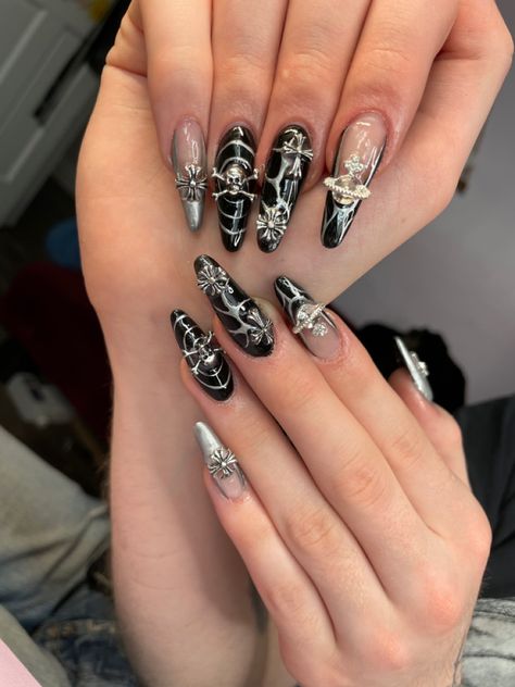 Long acrylic nails painted black with silver details and charms Acrylic Nails Rockstar Girlfriend, Black Nails Charm, Heavy Metal Inspired Nails, Emo Nails Y2k, Grunge Nails With Charms, Black Nail Designs Emo, Black Nail Designs Y2k, Goth Charm Nails, Nail Rock Style