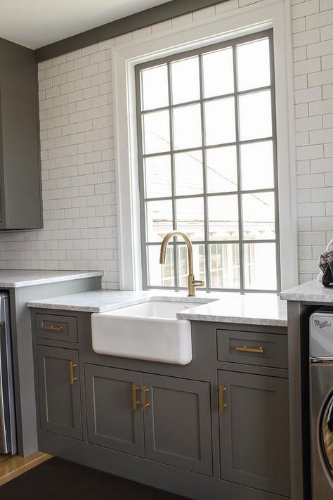 Charcoal gray laundry room features charcoal gray shaker cabinets adorned with long brass pulls is topped with carrera marble fitted with a farmhouse sink and a brass gooseneck faucet. Farmhouse Sink Laundry, Laundry Room Island, Gray Laundry Room, Contemporary Laundry Room, Gray Shaker Cabinets, Sink Laundry Room, Georgiana Design, Grey Laundry Rooms, Trendy Farmhouse Kitchen