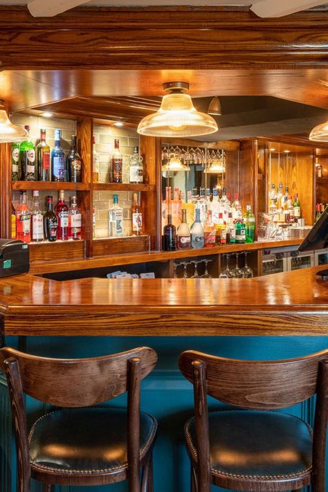 wooden polished bar front, alcoholic bottles out on display in shelves, blue bar front, wooden stools with back. Cosy Bedrooms, Rustic Beams, Diy Home Bar, Pub Chairs, Back Bar, Banquette Seating, The Pub, Stone Walls, Basement Bar