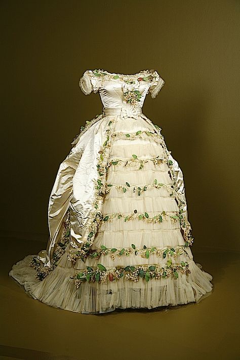 1869 wedding gown of Elisabeth of Wied, Queen Consort of Romania. Elisabeth's wedding dress shows the emergence of the bustle era. The flounces and over-skirt belong to the crinoline era. "The dress is made of silk satin, silk tulle with cotton and paper faux flowers." (via Fashion Institute of Design and Merchandising - Los Angeles, California USA). Historical Wedding, Historical Gowns, Queen Elisabeth, Queen Consort, Victorian Wedding, Silk Tulle, Antique Dress, Wedding Gowns Vintage, Vintage Gowns