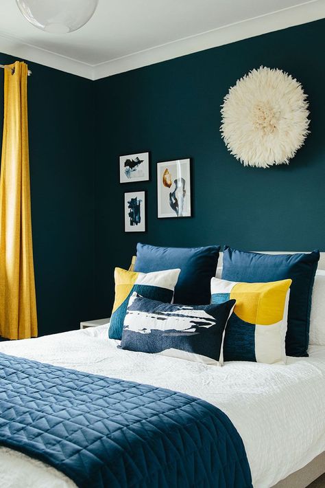 We love using dark blues to warm up a space. The pops of sunshine yellow in this bedroom scheme also add a welcome contrast and bring some energy back to the space - perfect for those mornings in the Autumn and Winter time where you might need a bit of encouragement out of bed! This room is so beautifully decorated that it could be a 5-star hotel room! Click the link to see how you can make your master bedroom so beautiful that you'll never want to leave! 🛏️ Bedroom Blue And Gold, Navy Yellow Bedrooms, Dark Blue Bedroom Walls, Blue Yellow Bedrooms, Mustard Bedroom, Teal Rooms, Dark Blue Bedrooms, Bright Bedroom, Blue Bedroom Walls