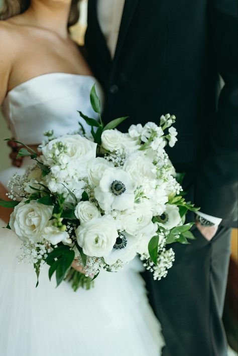 Close up photo of Bride holding a Bouquet filled with ivory roses, white anemone, ranunculus, babys breath, delphiniums and italian ruscus Bride Flower Bouquet White Anemones, White Roses And Anemones, Anemone Flower Bouquet Ranunculus, Black And White Anemone Bouquet, Bridal Bouquet White Peonies Ranunculus, White Bouquet With Anemones, Bridal Bouquet Classic Elegant, Italian Ruscus Wedding Bouquet, Big White Bouquet