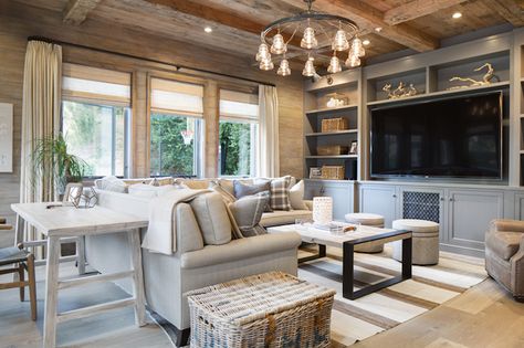 Rustic elegant living room features weathered wood planked ceiling accented with criss cross beams over wood planked walls which frame three windows layered in linen drapes and roman shades. The cottage living room boasts a light linen sectional dotted with gray plaid pillows across from a steel and wood coffee table and round poufs atop a ivory and beige striped rug. A distressed white sofa table doubling as desk stands behind the sectional facing a full wall floor to ceiling gray built-in me Elegant Living Room Furniture, Behind Couch, West Home, Cozy Living Spaces, Cottage Living Rooms, Coastal Living Rooms, Elegant Living Room, Family Room Design, Sofa Home