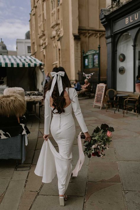 Bride in open back detailed long sleeve wedding dress with buttons down the middle and large white bow hair accessory walking to her wedding first look