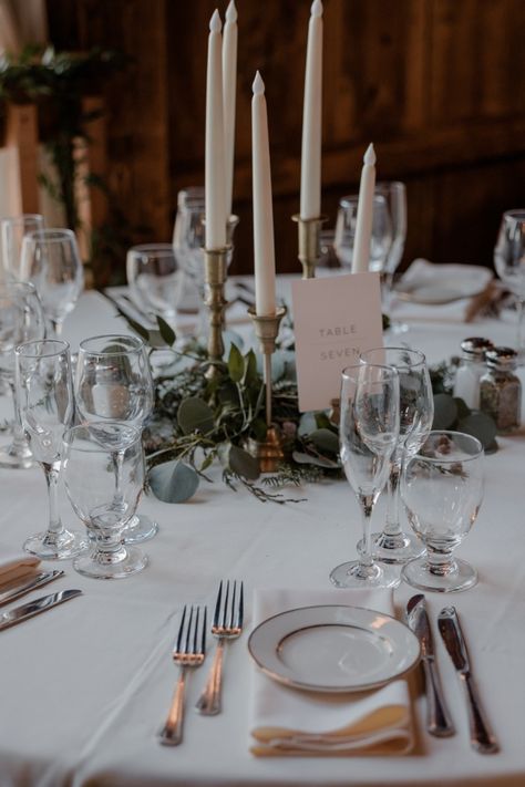 Simple, stunning table setting, white tablecloths, napkins, table number cards, beautiful greens and candles as centerpieces, Wedding, The Barns at Wesleyan Hills Candlestick Tablescape, Wedding Table Candlesticks, Taper Candle Centerpiece, Candlestick Centerpiece, England Winter, Rustic Elegant Wedding, Candle Wedding Centerpieces, Circle Table, Simple Elegant Wedding