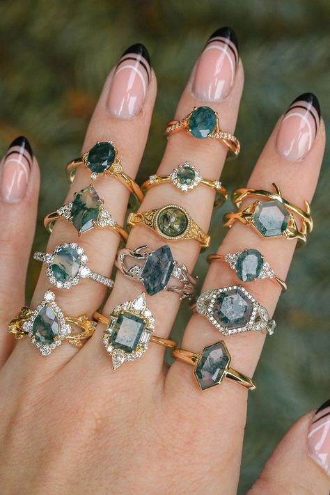 A woman's hand is shown wearing thirteen moss agate engagement rings from Staghead Designs. These rings are in 14K white, yellow, & rose gold & a variety of designs that include solitaires, halo engagement rings, & more. Agate Wedding Ring, Moss Agate Jewelry, Agate Wedding, Alternative Wedding Rings, Staghead Designs, Cute Engagement Rings, Future Engagement Rings, Agate Engagement Ring, Moss Agate Ring