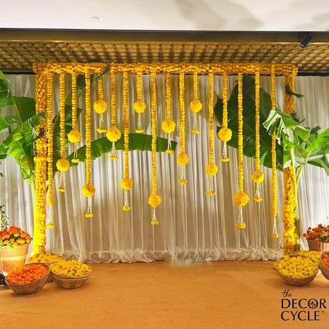 Simple and elegant South Indian Haldi Decor with genda phool and banana leaves. Backdrop Decoration. #southindian#haldi#mehendi#wedding#indianwedding#yellow#orange#genda#haldidecor#thedecorcycle Haldi Decoration Ideas At Home Terrace, Yellow Backdrop Decorations, Simple Haldi Decoration At Home Terrace, South Indian Haldi Decor, Rice Ceremony Decoration Indian, Haldi Ceremony Decorations Indoor, Pasupu Decor, South Indian Haldi, Indian Haldi Decor