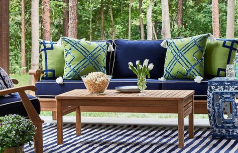 Patio features a teak sofa lined with blue cushions with white piping lined with green and blue pillows facing a teak coffee table atop a blue striped rug. Green And Blue Pillows, White Patio Furniture, Green Outdoor Pillows, Contemporary Deck, Small Patio Furniture, Blue Patio, Teak Sofa, Porch Furniture, Alfresco Dining