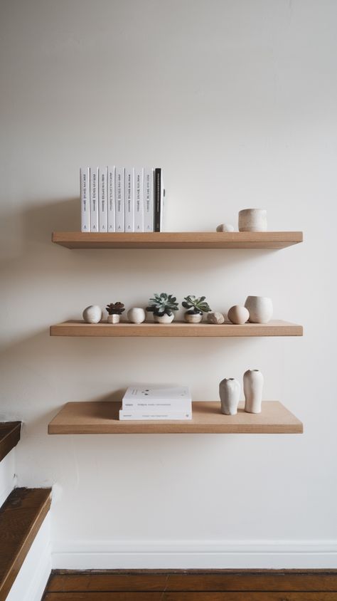 Light, natural wood floating shelves provide a clean, airy aesthetic. Decorate with small potted plants, ceramic pieces, and neutral-toned books for a cozy yet modern vibe. #WoodenDecor #MinimalHome #BiophilicDesign | Minimalist floating wooden shelves adorned with small succulents, neutral ceramics, and white books against a white wall Neutral Ceramics, Natural Wood Floating Shelves, Floating Wooden Shelves, Airy Aesthetic, White Books, Wood Floating Shelves, Small Potted Plants, Ceramic Pieces, Small Succulents