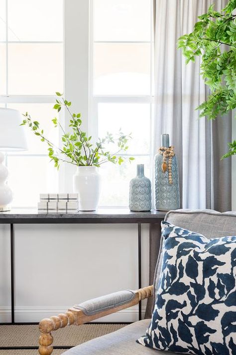 Black marble and iron console table under a living room window dressed with gray sheer curtains. Console Table Under Window, Table Under Window, Black Marble Console, Gray Sheer Curtains, French Console Table, Reclaimed Wood Mirror, Brass Console Table, Blue Vases, White Wainscoting