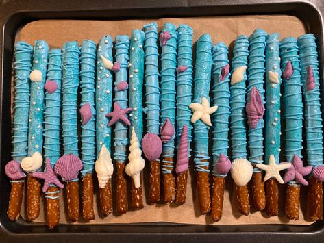 Baby blue chocolate covered pretzel rods with white and lavender seashells Shark Pretzel Rods, Mermaid Pretzel Rods, Ocean Pretzel Rods, Ocean Theme Deserts, Ocean Chocolate Covered Strawberries, Under The Sea Chocolate Covered Pretzels, Seashell Chocolates, Chocolate Pretzel Rods, Bday Decor