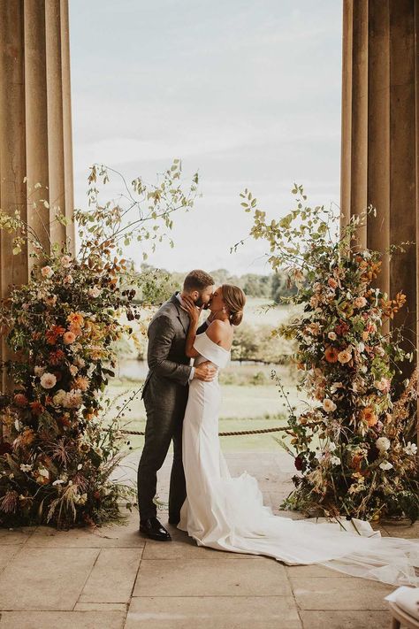 Bride and groom kiss inbetween pillars with orange, peach and white flower column altar decorations Flores Do Altar, Flower Columns, Wedding Altar Decorations, Altar Flowers Wedding, Wedding Columns, Alter Flowers, Wedding Pillars, Diy Wedding Arch, Flower Backdrop Wedding