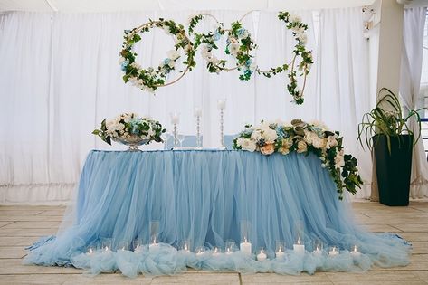 Produce a serene wedding table setup that will take your breath away with a stunning dusty blue two-layered tulle and satin table skirt that creates a soft and dreamy ambiance. Take in the beautiful gold metal hoops adorned with faux ivory, baby blue and white silk roses, bringing a touch of romance to the space. Let the faux white, baby blue and ivory silk roses on the table add a delicate touch of beauty to your table. Bask in the gentle glow of the white flameless votive candles displayed on Event Decor Ideas, Party Decorations Table, Wedding Table Setup, Wedding Arbors, Flowers Candles, Decorations Table, Candle Displays, Table Skirt, Ivory Silk