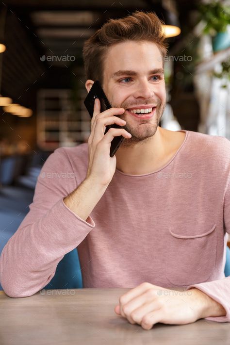 Attractive smiling young man talking on mobile phone by vadymvdrobot. Attractive smiling young man talking on mobile phone while sitting at the cafe table indoors #AD #man, #talking, #mobile, #Attractive Talking On Phone, Cafe Table, Talking On The Phone, The Cafe, On Phone, Male Poses, Design Diy, Business Card, Card Design