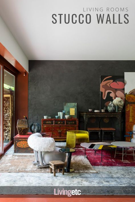 This space is a vibrant overlaying of African artefacts with contemporary furniture and photography, set against black stucco walls and clay-red resin flooring. #greywalls #stuccowalls #livingrooms Stucco Interior Walls Ideas, Interior Walls Ideas, Stucco Interior, Stucco Interior Walls, Black Stucco, Resin Flooring, Walls Ideas, Long Living Room, Stucco Walls