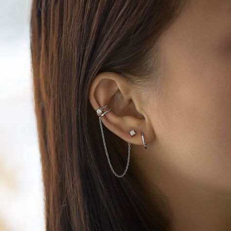 A unique conch ear cuff that features a chain and connected stud earring. Bendable for a snug fit. Sold as a single earring. Sterling Silver Cubic Zirconia, prong setting Hypoallergenic, lead and nickel free Inner diameter 9mm x Band Thickness 1.5mm Crystal 3mm Chain Length 2.75in Bendable for a snug fit #E515-Sx1 Piercings Oor, Unique Ear Cuffs, Minimalist Ear Piercings, Different Ear Piercings, Unique Ear Piercings, Ear Peircings, Earring Cuff Chain, Ear Cuff Chain, Types Of Ear Piercings