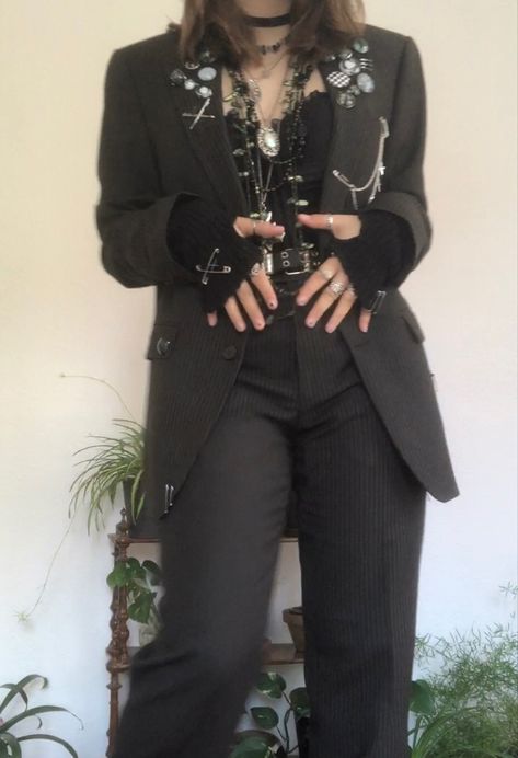 A mid-sized person/girl grey/dark green striped suit decorated with lots of oins and chains, black arm warmers, black platform dr. Martens and multiple crystal rings and bracelets. 		The person is also wearing multiple silver necklaces, a big one in form of a cross. Alternative Semi Formal, Aesthetic Suit Outfit, Corset And Suit Outfit, Alt Suit Outfit, Punk Prom Suit, Alt Suit Aesthetic, Punk Blazer Outfit, Punk Corset Outfit, Masc Goth Outfits Formal