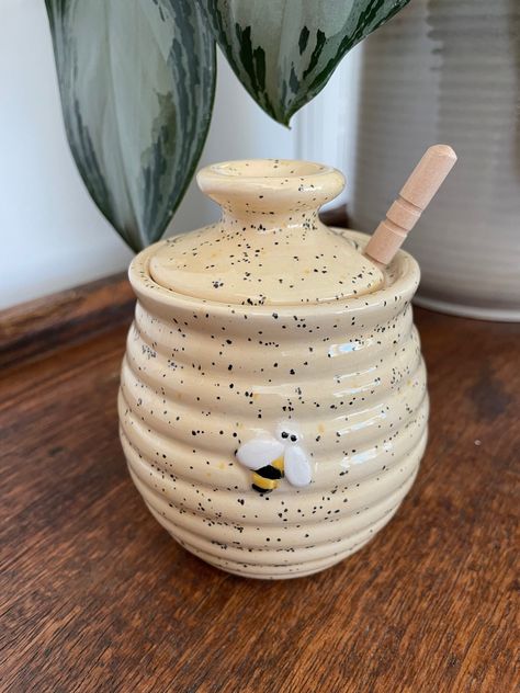 This beautiful ceramic honey pot features horizontal ridges to create a beehive effect, a hand painted bee design and a simple lid with a stopper. Use its traditional dibber to effortlessly drizzle honey over all your favourite foods.  It has been hand painted using honey toned speckle underglaze paints and then glazed and fired in my studio kiln.  Dimensions: Pot & Lid:  11cm (H) x 9cm (W) x 9cm (D) Dibber: 11.5cm (H) x 2cm (D) Thank you for taking the time to look at my range. It really does mean a lot. Honey Pot Pottery, Ceramic Honey Jar, Pottery Honey Pot, Ceramic Honey Pot, Personalized Birthday Plate, Honey Pots, Birthday Plate, Bee Inspired, Custom Plates