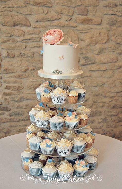 A pretty peach, blue and lacy cupcake tower for one of today's weddings. A sugar rose with blue and peach butterflies on the top cake with a variety of cupcakes. All set up at the lovely The Kingscote Barn - Wedding venue. Blue Wedding Cupcake Tower, Blue Wedding Cupcakes, Diy Wedding Cupcakes, Kingscote Barn, Wedding Cake Peach, Cupcake Towers, Cupcake Tower Wedding, Cupcake Wedding, Grad Cake