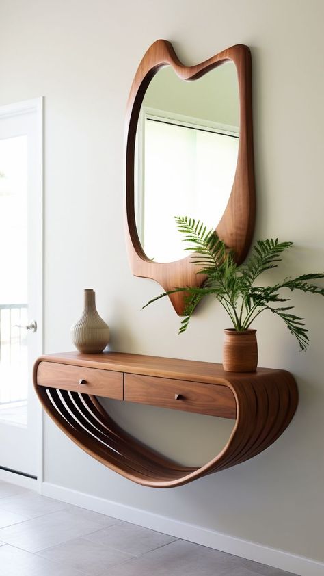 A wall-mounted console table and mirror set. The console table has an organic, curved design resembling a wave or a ribbon, with a flat surface on top for placing objects and an open shelf area underneath. It is made of wood with a rich, warm tone that complements the similarly styled wooden frame of the mirror above it. The mirror has an asymmetrical shape, wider at the top and tapering towards the bottom. By freepik Tiny Front Entry, Small Apartment Entrance, Small Entryway Decor Ideas, Apartment Entryway Decor, Console Table And Mirror, Small Open Concept, Mid Century Modern Entryway, Mid Century Entryway, Entryway Inspo