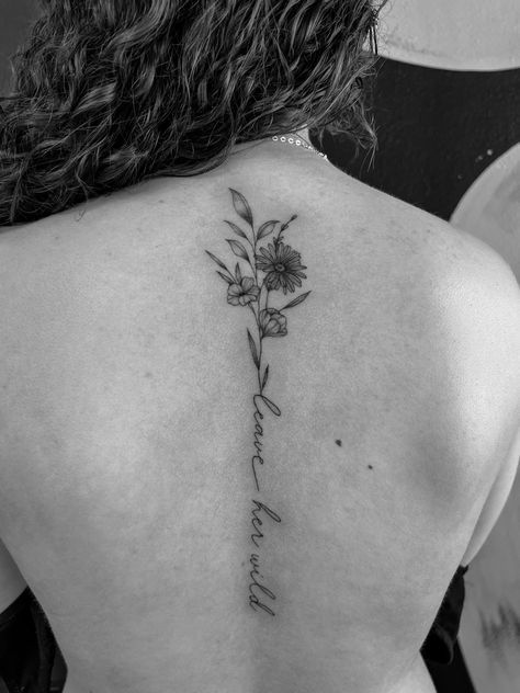 Spine tattoo, leave her wild, wildflowers, fineline Beautiful Spine Tattoos, Strength Spine Tattoos For Women, Cursive Tattoos With Flowers, Flower And Writing Spine Tattoo, Spine Tattoo With Words, Spine Tattoo Quotes With Flowers, Spine Bouquet Tattoo, Aster Flower Spine Tattoo, Flowers With Quotes Tattoo