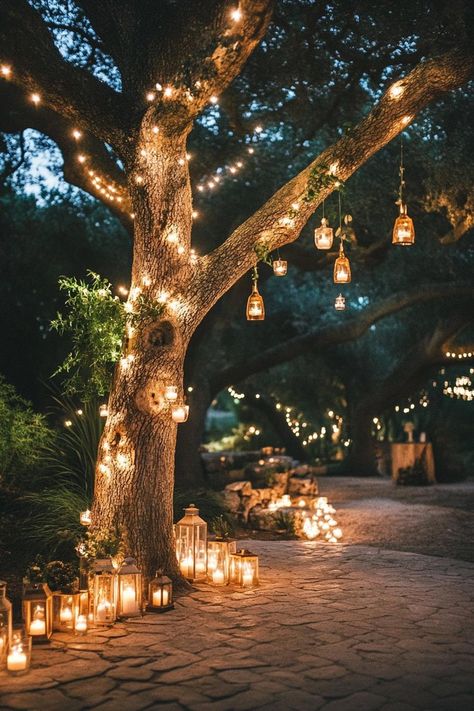 Enchanted forest theme wedding outdoor decor with a tree decorated with fairy lights and tiny lanterns under the tree there is a paved ground lined. Let your big day become a magical woodland affair with these enchanting forest wedding ideas that’ll make your guests feel like they’ve stepped into a fairy tale. Wedding Fairy Aesthetic, Tree Lanterns Wedding, Forest Wedding Photo Booth, Jewel Tone Enchanted Forest Wedding, Practical Magic Themed Wedding, Cabin Wedding Decorating Ideas, Tolkien Wedding Decor, Gothic Woods Wedding, Backyard Fairy Wedding