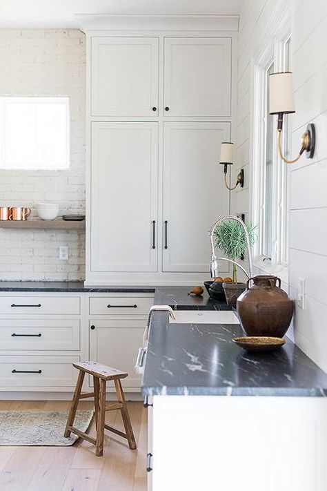 White kitchen cabinets contrasted with oil rubbed bronze pulls and a honed soapstone countertop are fitted with a sink paired with a pull out faucet mounted in front of a window framed by white shiplap and flanked by Elkins Sconces. Soapstone Kitchen, White Shaker Kitchen Cabinets, Bronze Pulls, White Shaker Kitchen, Soapstone Countertops, Shaker Style Cabinets, Shaker Kitchen Cabinets, Home Luxury, Kitchen Views